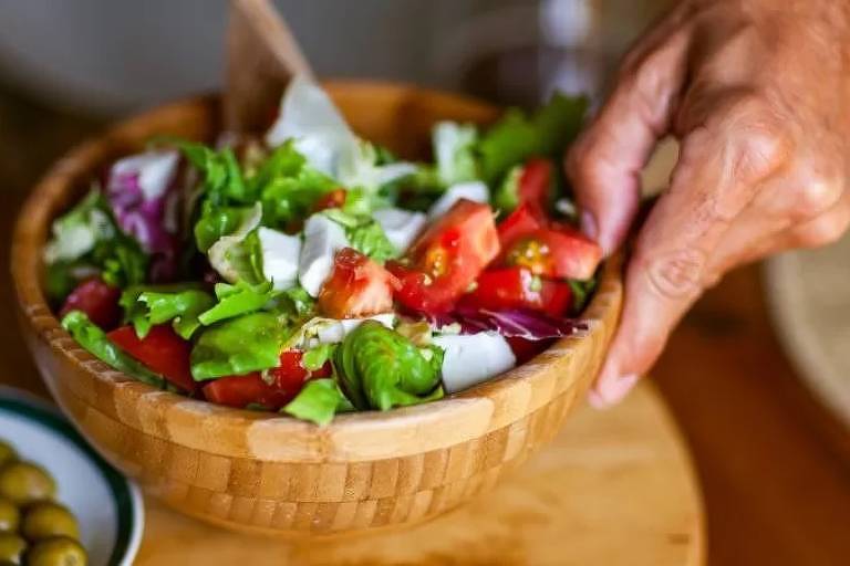 Imagem em close mostra a mão de uma pessoa segurando um recipente com salada dentro