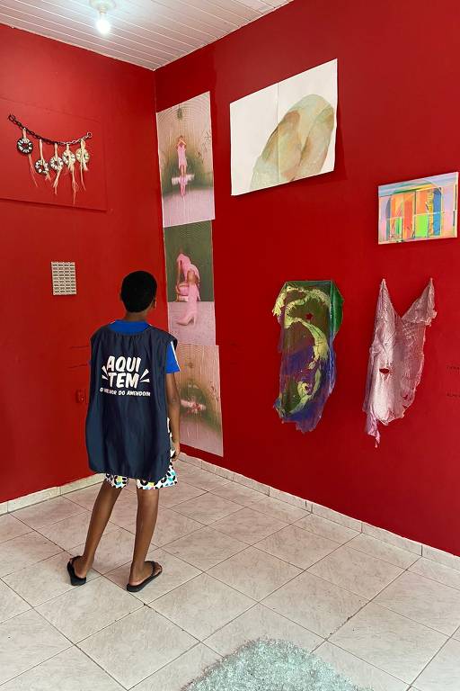 Foto de parede vermelha de galeria com obras de arte; uma criança vê as obras à esquerda