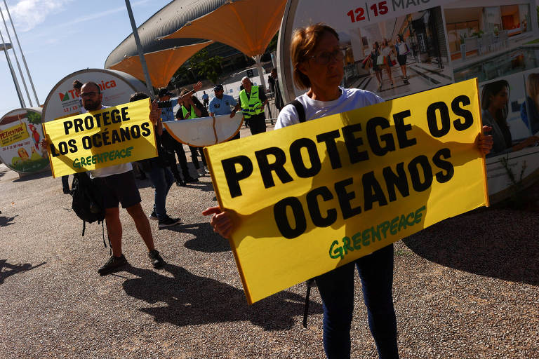 Duas pessoas seguram cartazes amarelos que dizem "protege os oceanos"