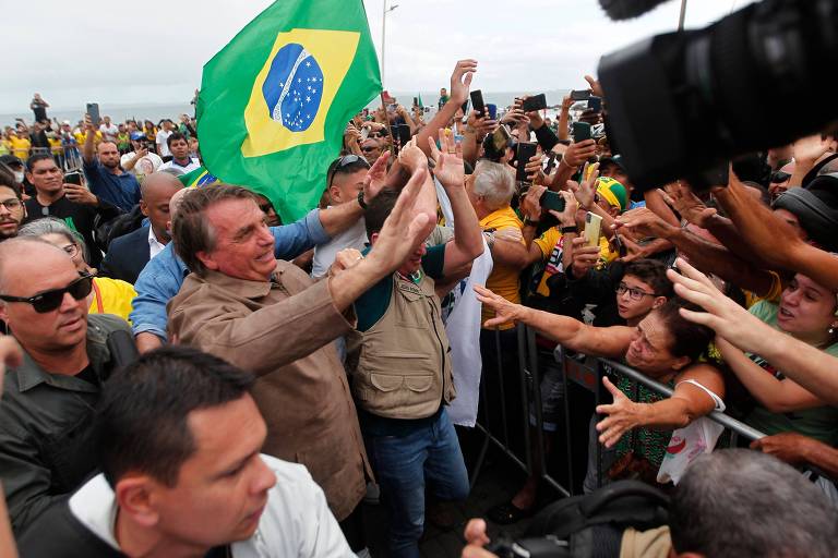 Bolsonaro é cercado por multidão; um pouco atrás dele, uma bandeira do Brasil