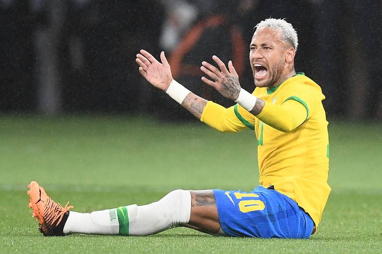Sentado no gramado e com os braços estendidos, Neymar reclama da arbitragem em amistoso do Brasil com o Japão; ele usa camisa amarela, calção azul e meias brancas