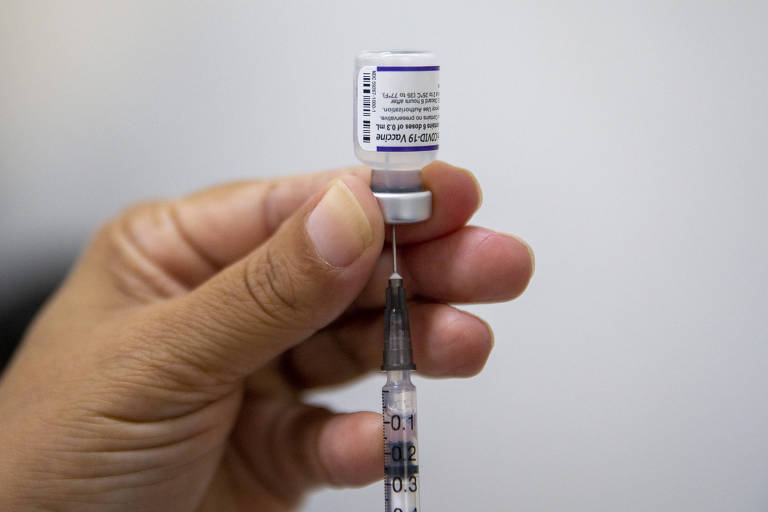 Foto destaca mão de enfermeira segurando seringa com frasco de vacina