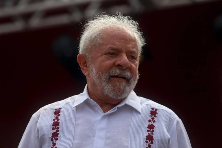 Imagem mostra Lula, vestindo camisa branca com flores vermelhas como detalhes, olhando para o lado