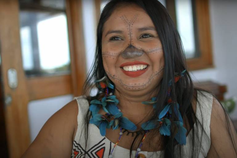 mulher indígena com desenhos corporais sorri em ebarcação