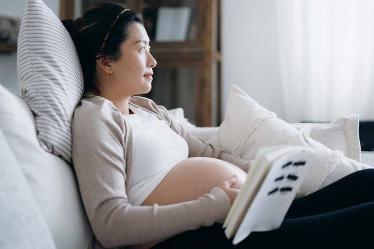 Mulher grávida sentada de lado no sofá