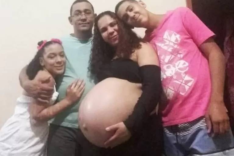 Imagem em primeiro plano mostra mulher grávida posando para foto ao lado do marido e do casal de filhos
