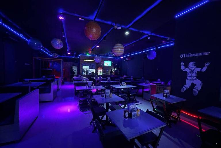 Ambiente da hamburgueria Burger Espacial, na Mooca, com temática de ETs e espaço