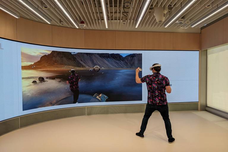 Em uma sala ampla da Meta Store, um homem está de costas; diante dele, uma tela grande mostra o cenário que ele vê com os óculos de realidade virtual: uma paisagem natural e montanhosa, como se estivesse navegando no mar com um barco