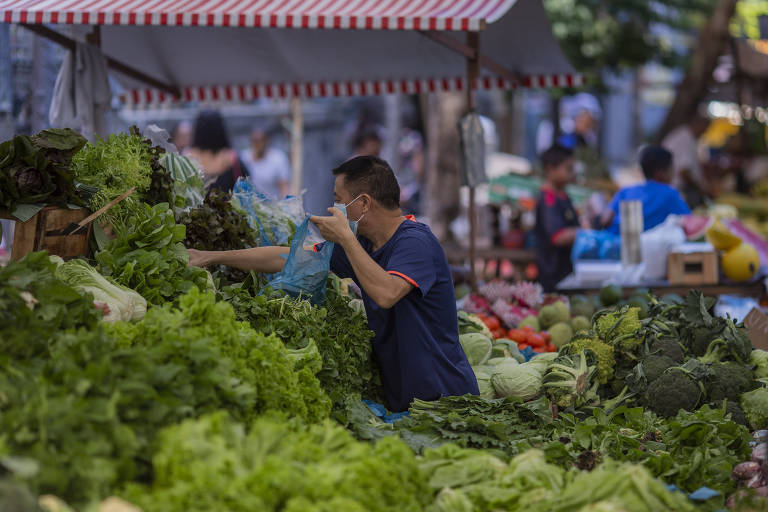 Homem faz compras em banca de verduras em feira livre