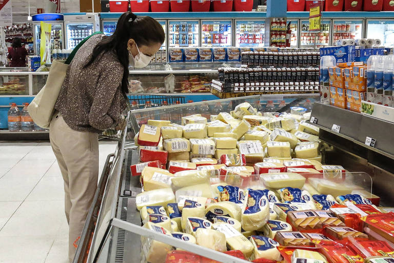 Mulher observa queijos em geladeira de supermercado