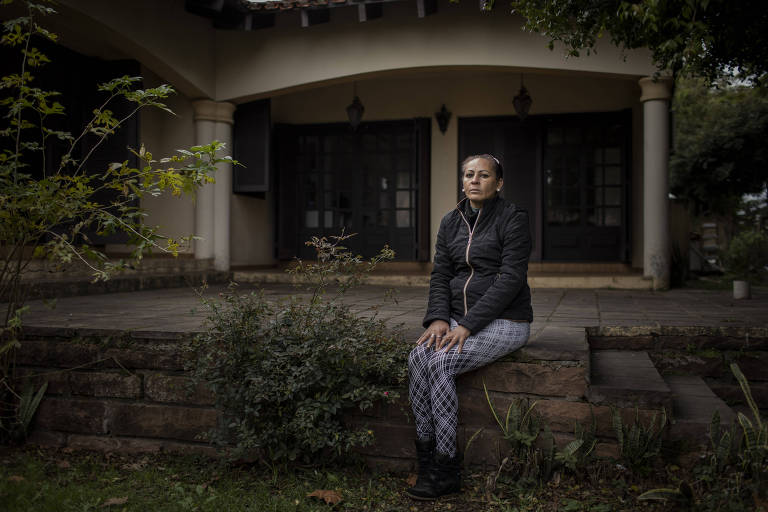 Mulher negra sentada em um pequeno muro de pedras olha para a câmera, com as mãos sobre as pernas