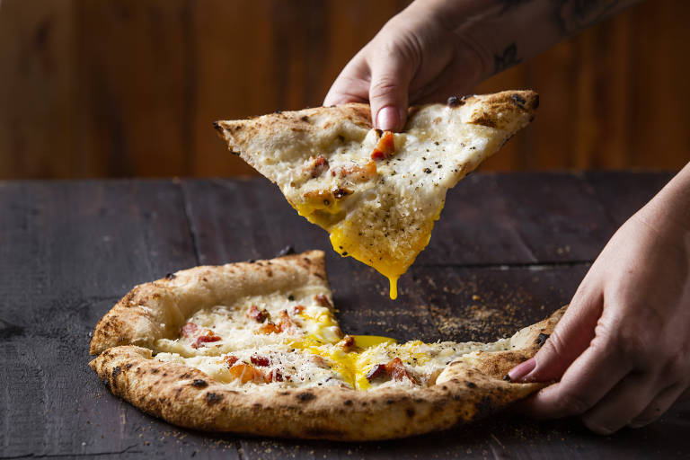 Pizza em cima de superfície cinza escuro. Mão branca tira um pedaço