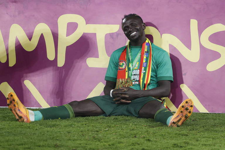 O atacante Sadio Mané sorri, sentado no gramado com as pernas abertas, depois de o Senegal superar o Egito e conquistar pela 1ª vez a Copa Africana de Nações