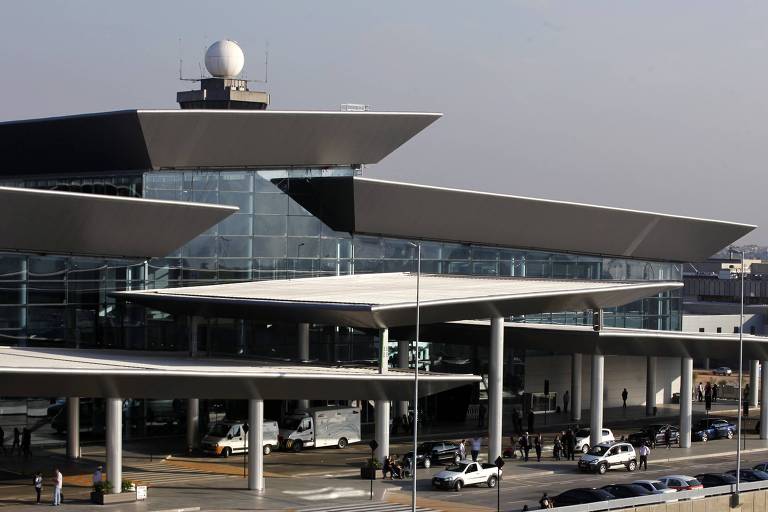 Prédio do aeroporto com muitos carros e pessoas entrando e saindo do terminal