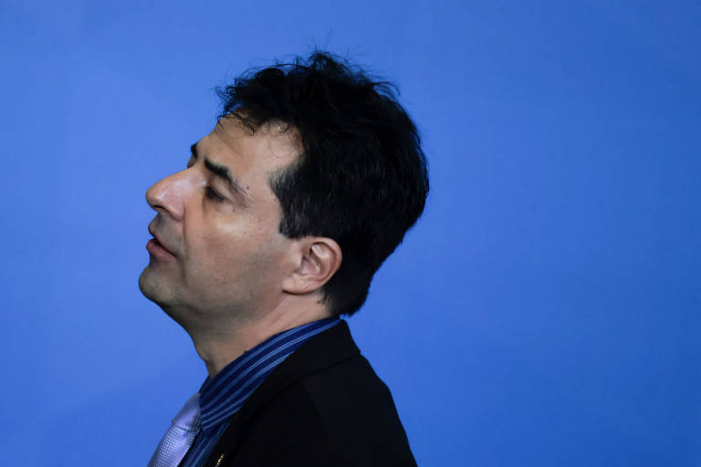 Imagem mostra perfil de Adolfo Sachsida. Ele usa um terno preto com camisa azul. O fundo é azul.