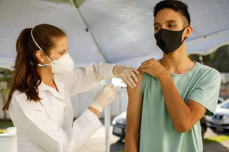 Imagem em primeiro plano mostra um garoto sendo vacinado por uma profissional da saúde