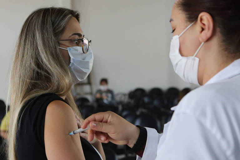 Enfermeira vacina uma mulher de máscara contra a Covid-19