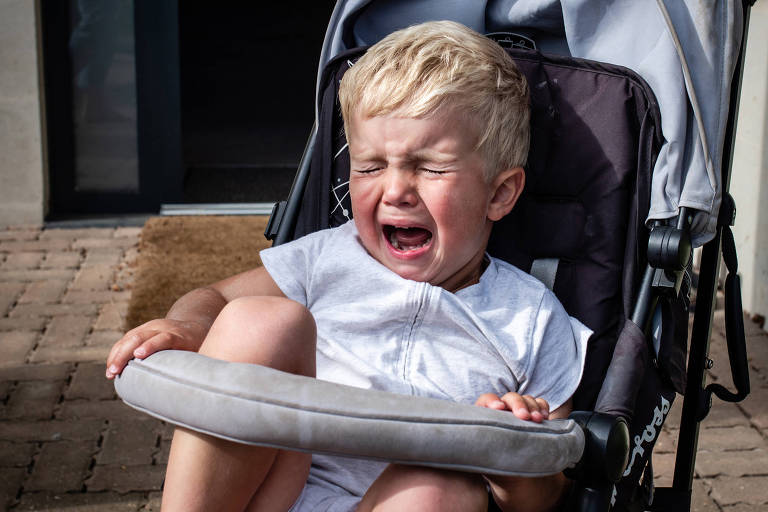 Criança loira sentada no carrinho chorando