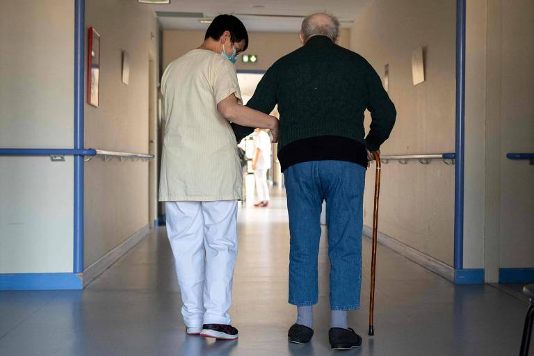 Enfermeira ampara homem idoso em corredor de hospital