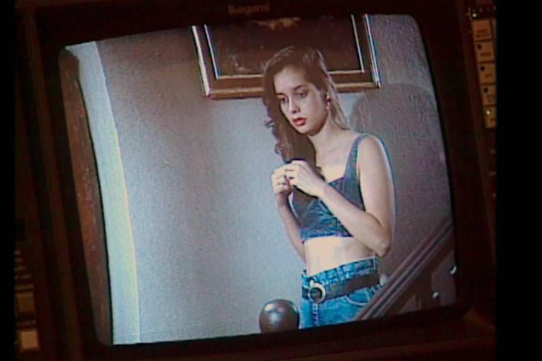 Jovem garota branca usa uma bluza azul numa cena de novela