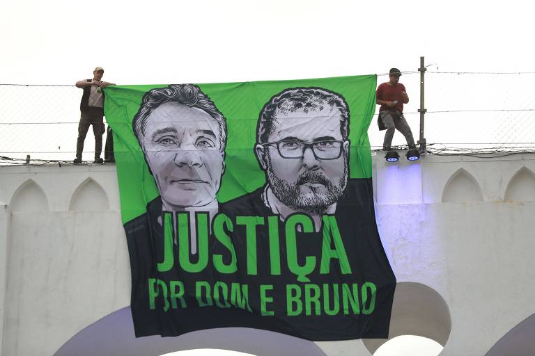 Imagem mostra manifestantes com bandeira com rostos de Bruno e Dom em cima dos arcos da Lapa
