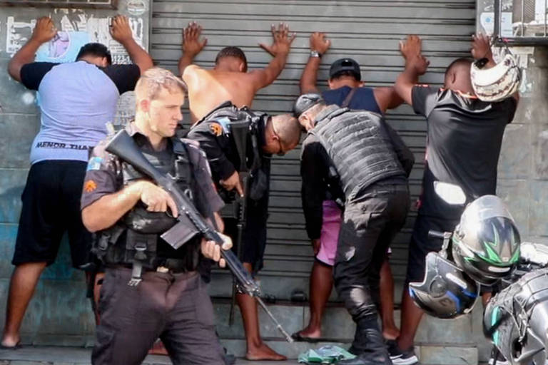 homens de costas com maos pra cima sendo revistados por policiais