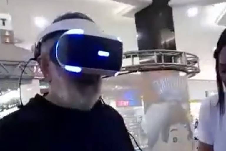 Em foto colorida, um homem de blusa preta se diverte com óculos de  realidade virtual em shopping