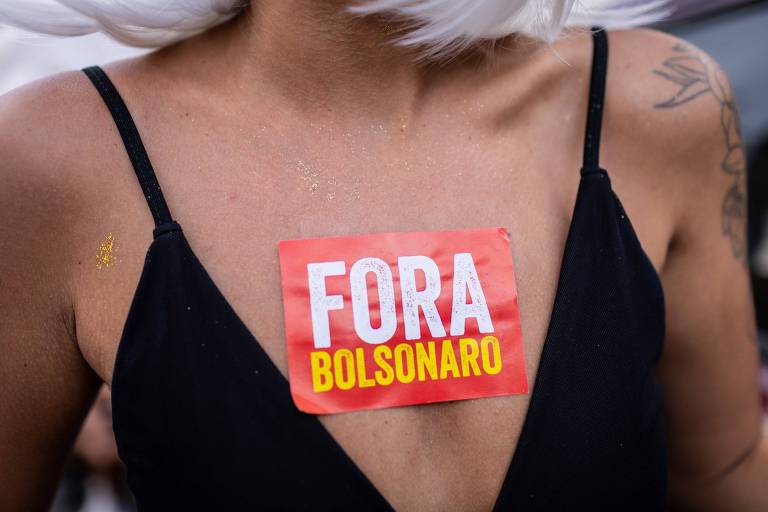 Torso de foliona, de blusa de alcinhas preta, com um adesivo escrito "Fora, Bolsonaro" colado no decote