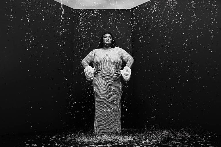 Uma mulher negra e gorda veste um longo vestido branco e posa para foto enquanto uma chuva leve cai sobre ela