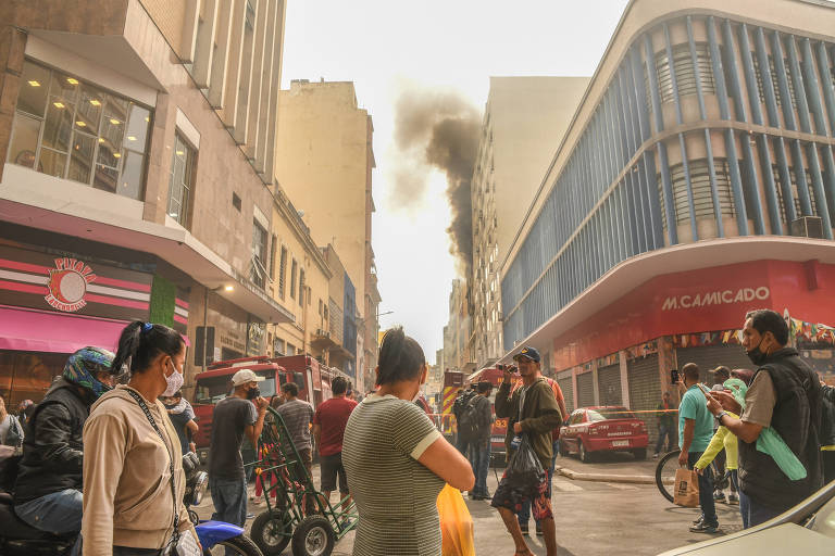 Pedestres observam a fumaça do incêndio no prédio na região da rua 25 de Março