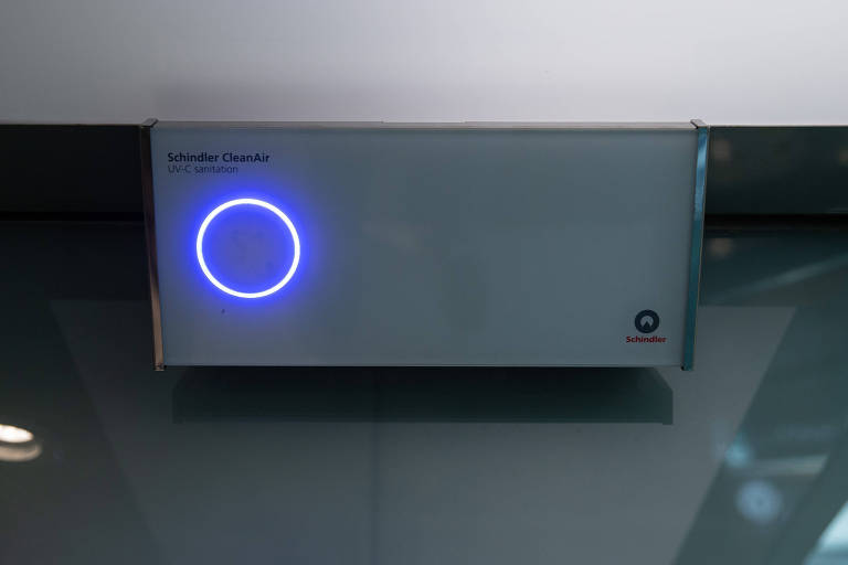 Imagem mostra esterilizador de luz UV. É uma caixa branca com um círculo iluminado.