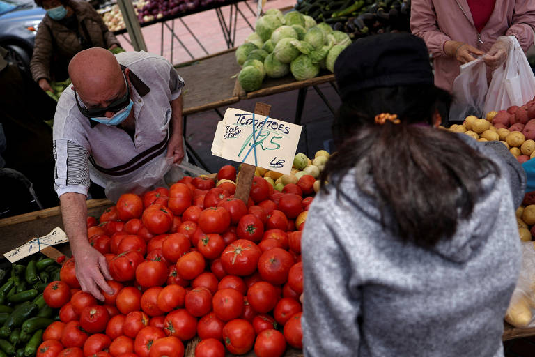 Vendedor de tomates é observado por cliente em mercado nos Estados Unidos 