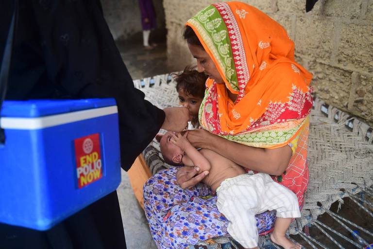 Funcionária do serviço de saúde do Paquistão administra gotas da vacina contra a poliomielite em criança da cidade de Karachi, em campanha porta a porta