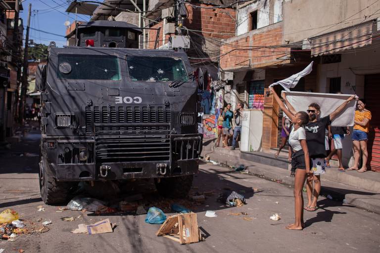 Moradores pedem paz durante protesto no Alemão em frente a blindado da polícia; segundo as polícias, 15 pessoas morreram em confronto, além do cabo Bruno de Paula Costa, 38, baleado enquanto estava trabalhando na base da UPP Nova Brasília, e a moradora Leticia Marinho, 50, que passava de carro pela região.