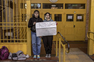 Agostina Fernndez Tirra and Luana Pereyra, LGBTQ rights activists, hold a sign using gender-neutral language in front of their school in Buenos Aires, Argentina, on June 30, 2022. (Sarah Pabst/The New York Times)