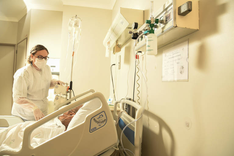 Imagem mostra enfermeira atendendo paciente em uma maca de um quarto de hospital