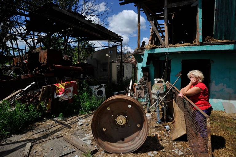 Mulher observa estado de sua casa atingida por bombardeio na vila de Zalissia, na região de Kiev, na Ucrânia