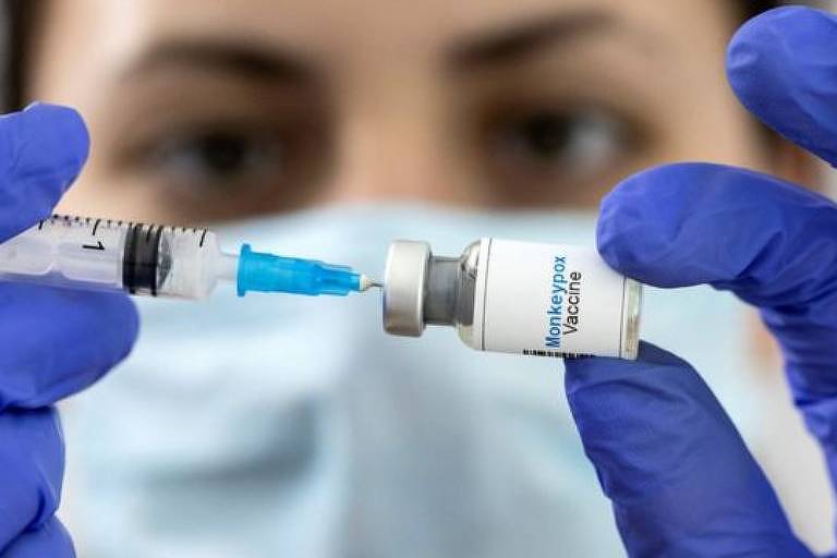 Imagem em close mostra as mãos de uma profissional da saúde espetando uma seringa em uma ampola de vacina