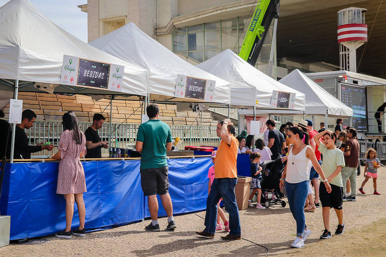 A foto mostra algumas barracas servindo comida com pessoas transitando pelo evento