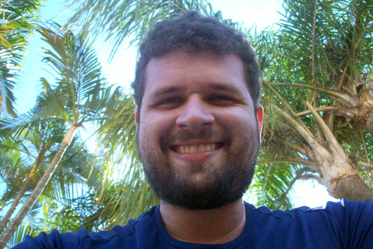 selfie de homem branco que sorri, com árvores ao fundo