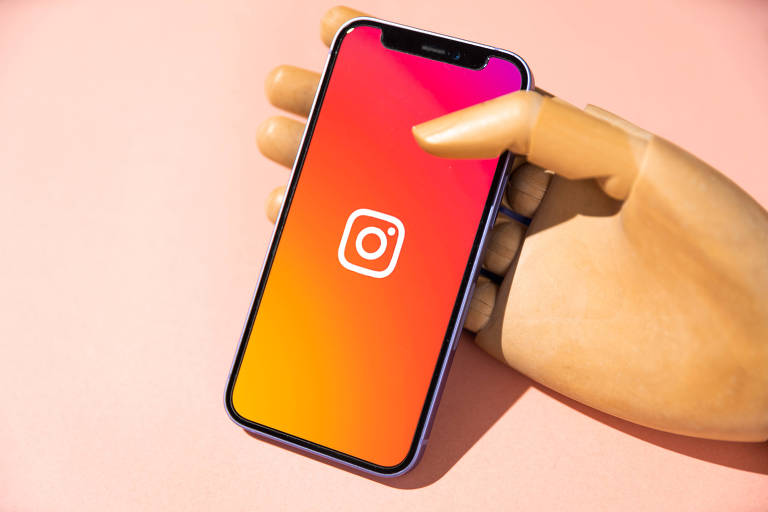 Mão de madeira segura celular com logo do Instagram
