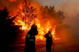 FILE PHOTO: Firefighters and volunteers try to extinguish a wildfire burning in Ntrafi, Athens