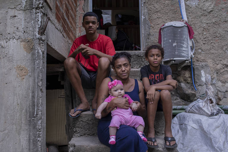 mulher com bebê no colo ladeada por dois meninos sentados todos em uma escada rebocada em uma casa sem reboco na favela no Rio