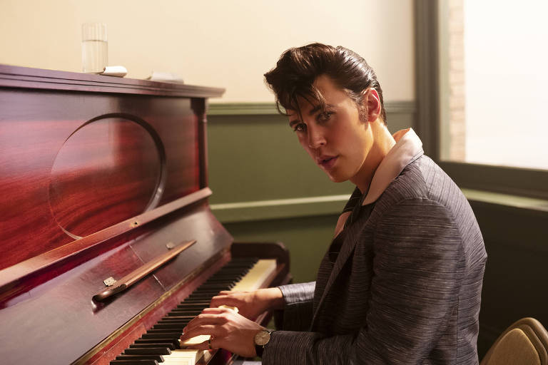 Em foto colorida, homem de terno toca piano em uma sala