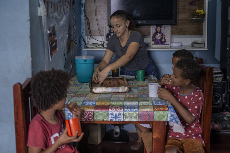 mulher dá comida para três crianças dentro de casa em favela