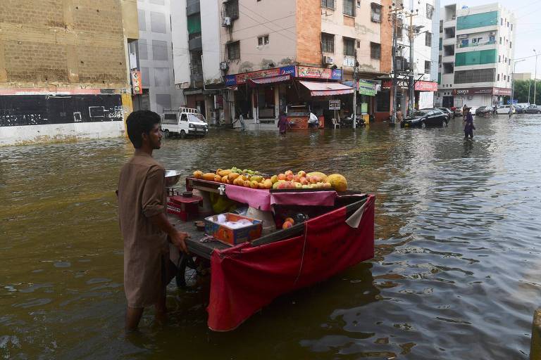 Vendedor de frutas passa por enchente em Karachi, no Paquistão, onde as chuvas de monção foram mais fortes que o esperado este ano