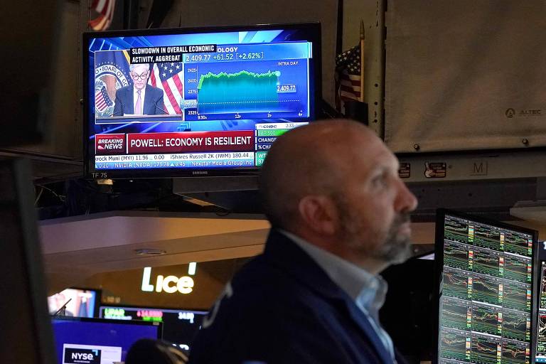 Operadores de mercado trabalham na Bolsa de Nova York enquanto televisor mostra discurso do presidente do Fed, Jerome Powell, nesta quarta-feira (27)