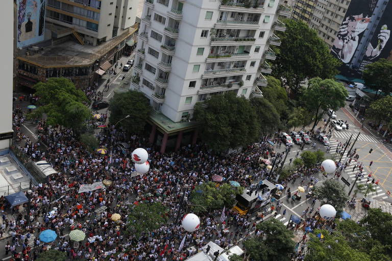 Imagem mostra multidão protestando em meio a prédios.