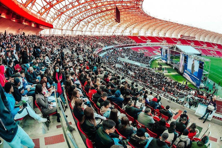 Estádio de futebol Beira-Rio, de Porto Alegre, com jovens estudantes na plateia e um palco no campo onde ocorre o evento Crie o Impossível