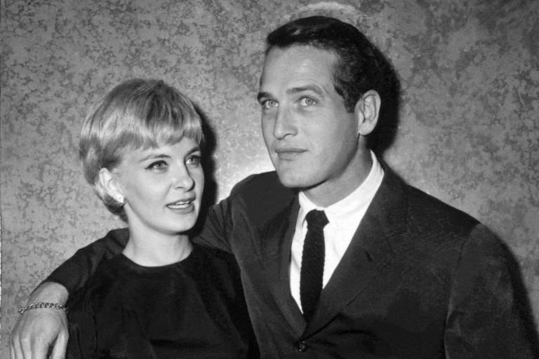 O casal de atores Paul Newman e Joanne Woodward em uma foto em preto e branco na qual Newman está com o braço direito no ombro de sua esposa, Woodward